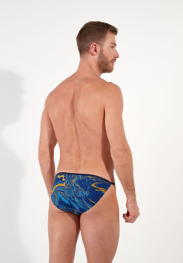 Man wearing blue tanga briefs with yellow abstract pattern on a white background